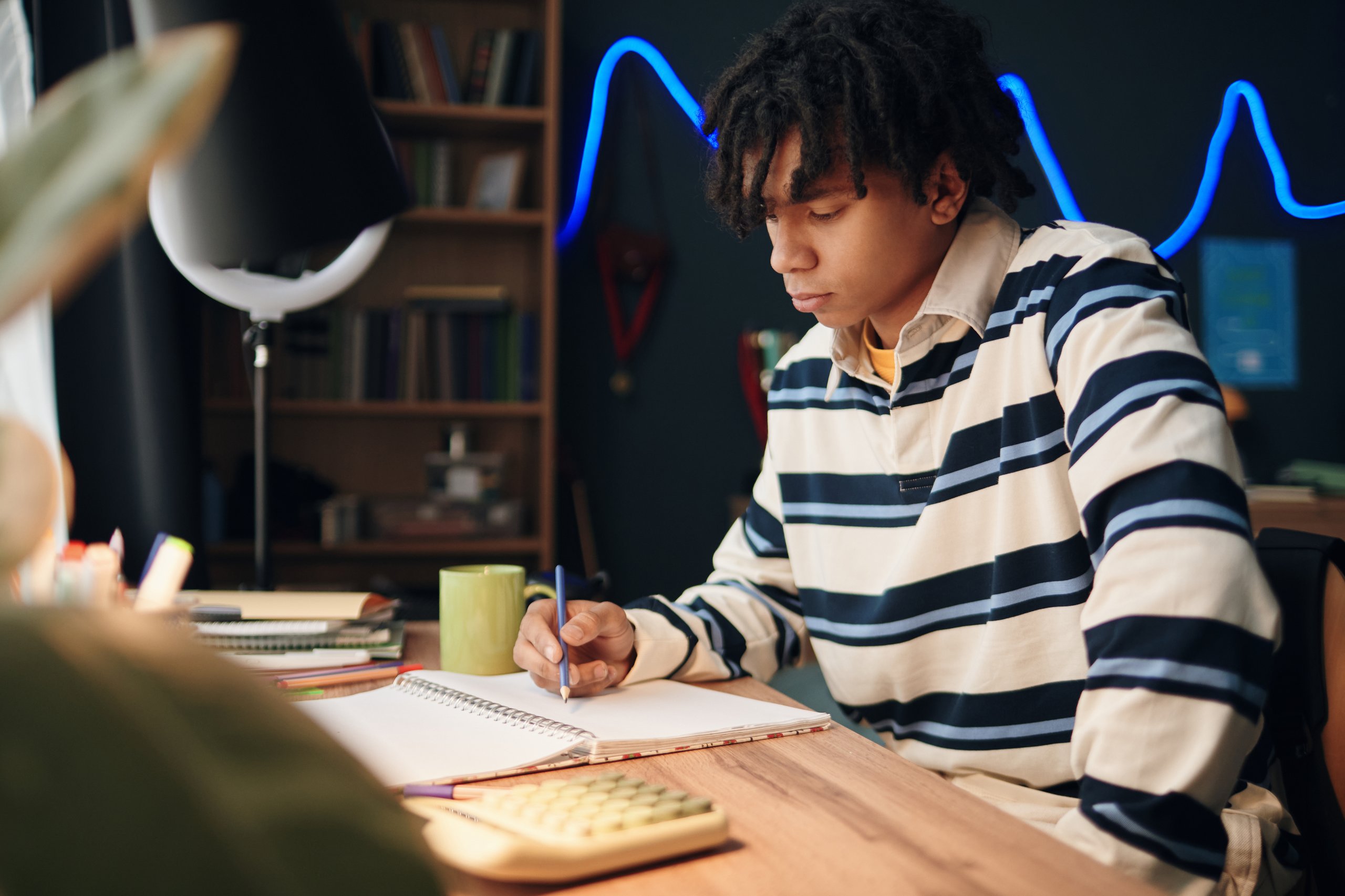 Teenage boy studying at desk with focused expression, educational support and personal development