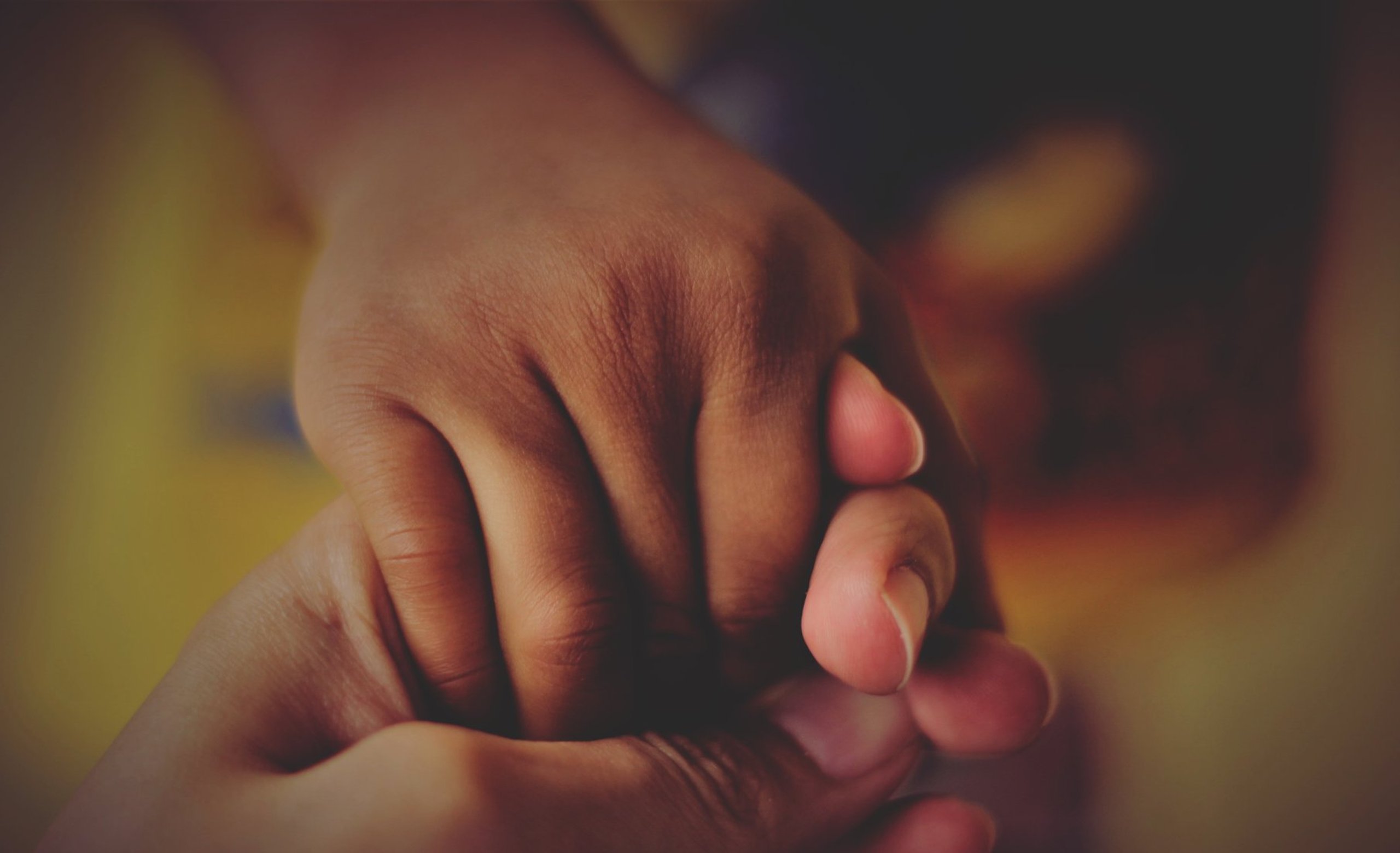 Adult gently holding child's hand, symbolizing protection, trust, and nurturing care