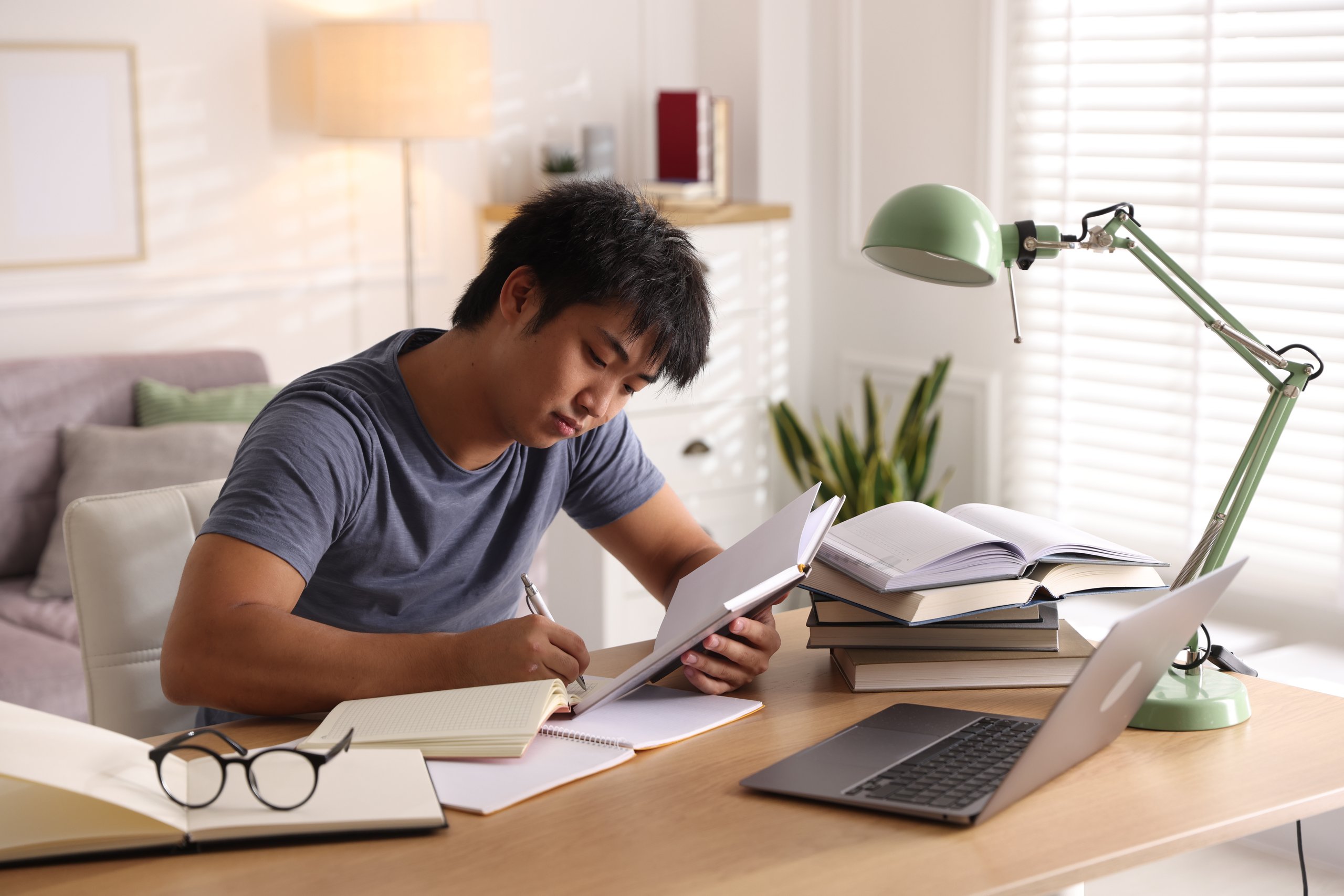 Young male student with laptop and books preparing for exam, educational support and studying