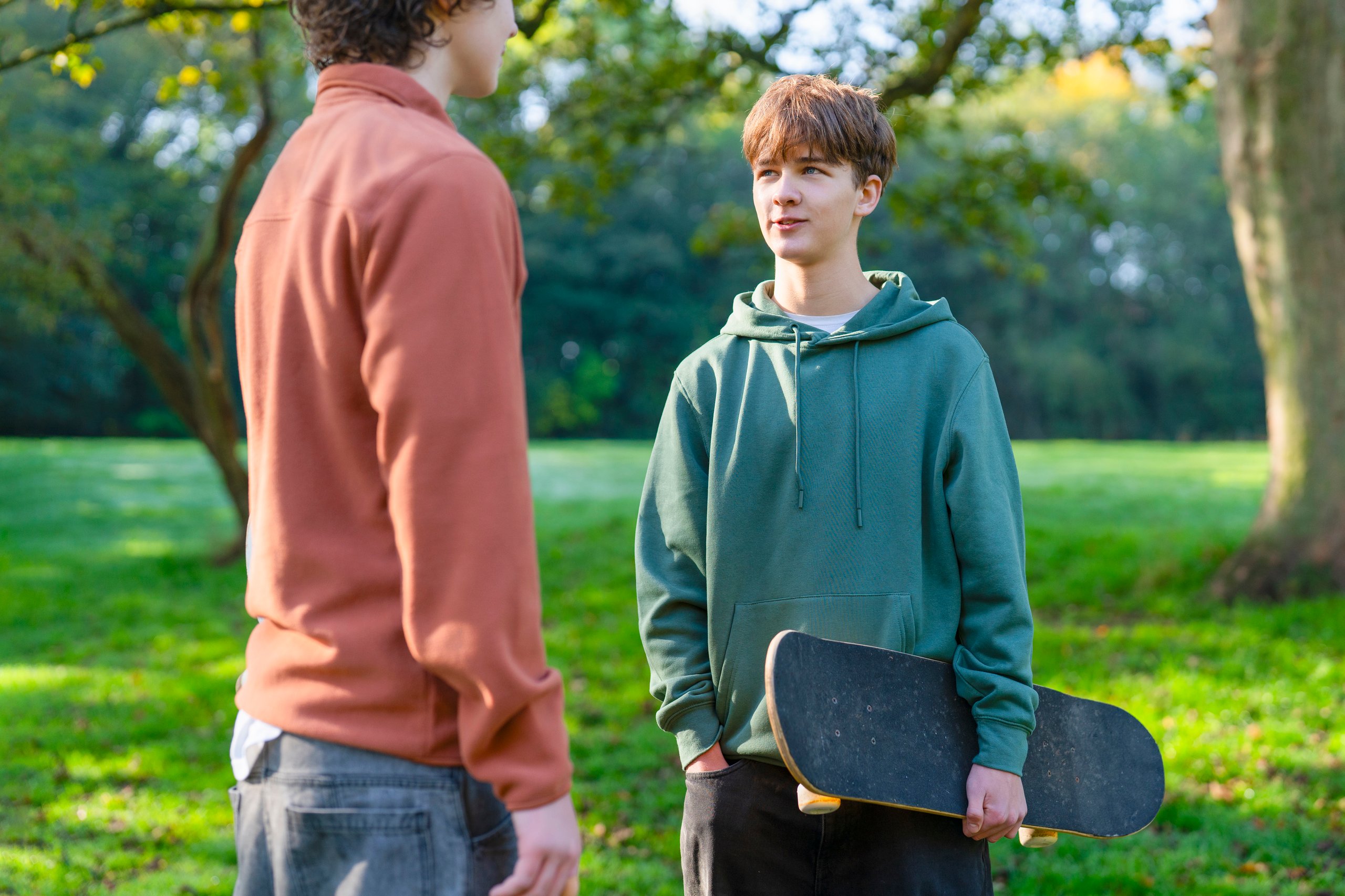 Two young males standing together outdoors in conversation, supportive friendship and engagement