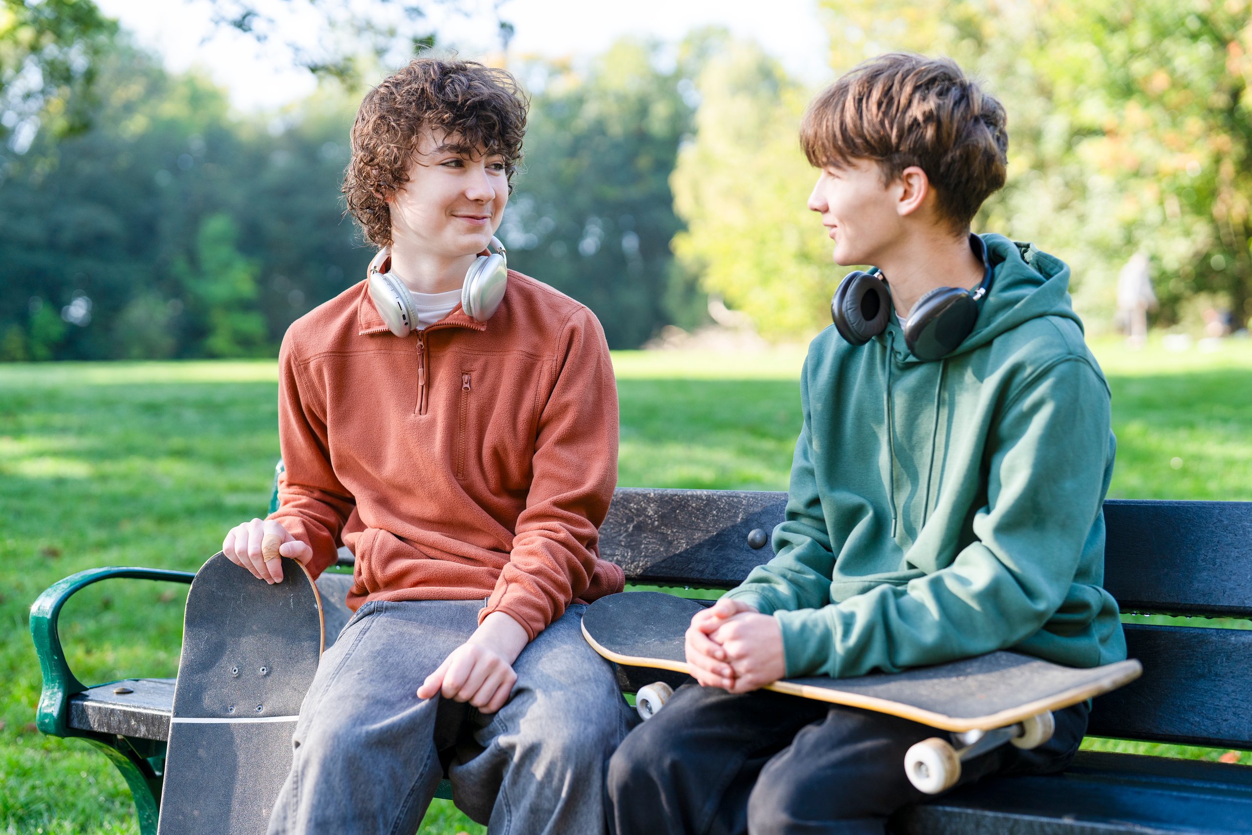 Two teenage boys sitting on a bench smiling and chatting together outdoors, positive friendship